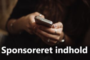 Kvindehænder med smykker holder mobiltelefon frem fra mørke