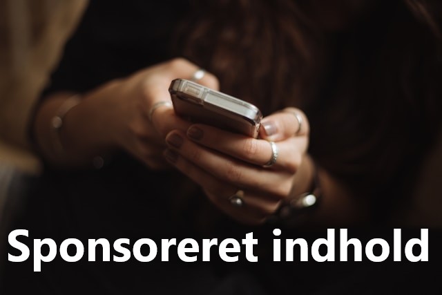 Kvindehænder med smykker holder mobiltelefon frem fra mørke